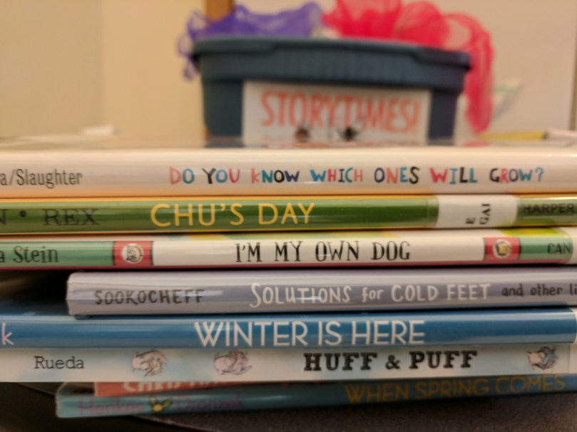 Stack of storytime books, with storytime box and scarves in the background