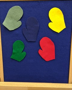 Five colored mittens on blue felt board