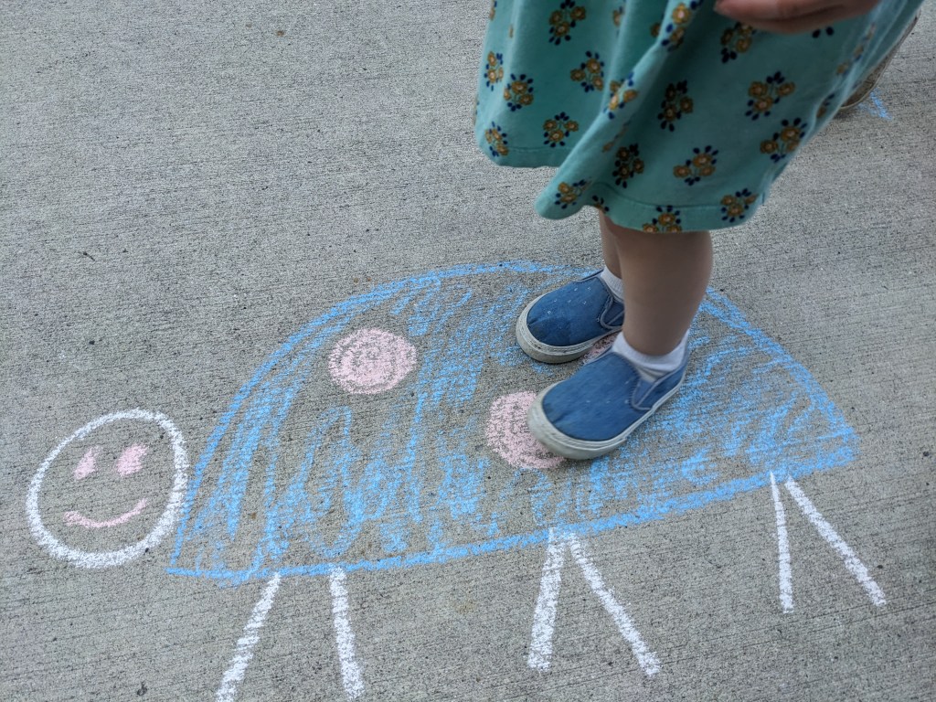 Child's legs and feet, standing on a smiling ladybug drawn in chalk