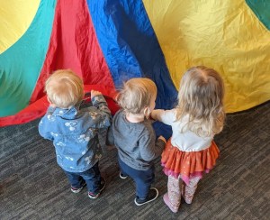 three small blond kids holding a parachute