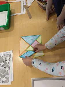 a pair of hands arranging tangrams into a square