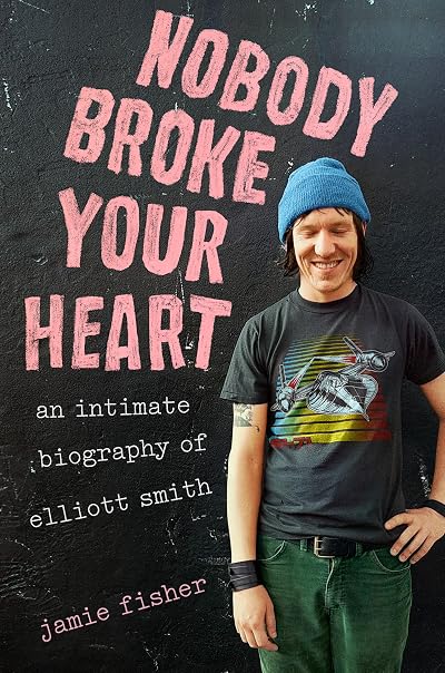 Cover of Nobody Broke Your Heart, with the title in pink all-caps text and a photo of Elliott Smith wearing a blue beanie, black wristband, and green pants